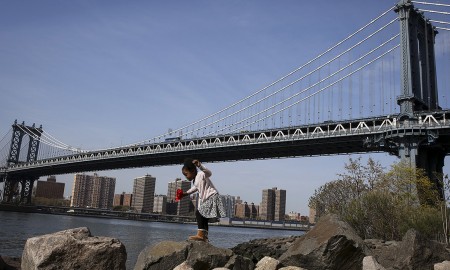 Uma criança brinca nas rochas sob a ponte de Manhattan no bairro de Brooklyn em Nova Iorque, EUA – CARLO ALLEGRI/REUTERS